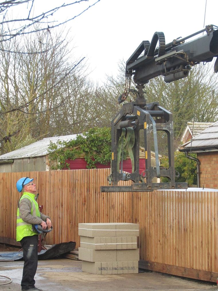 Une grue de camion dépose des blocs de béton sur le chantier ; un ouvrier la guide à la télécommande.